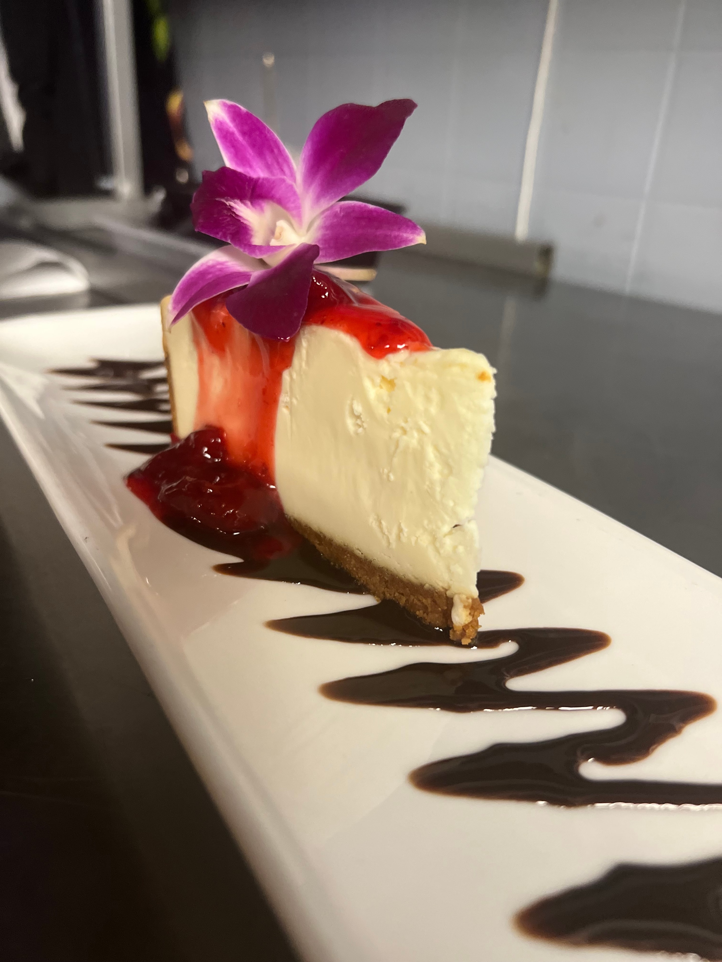 Strawberry cheesecake with orchid garnish and chocolate drizzle — Dr. Bea signature dessert