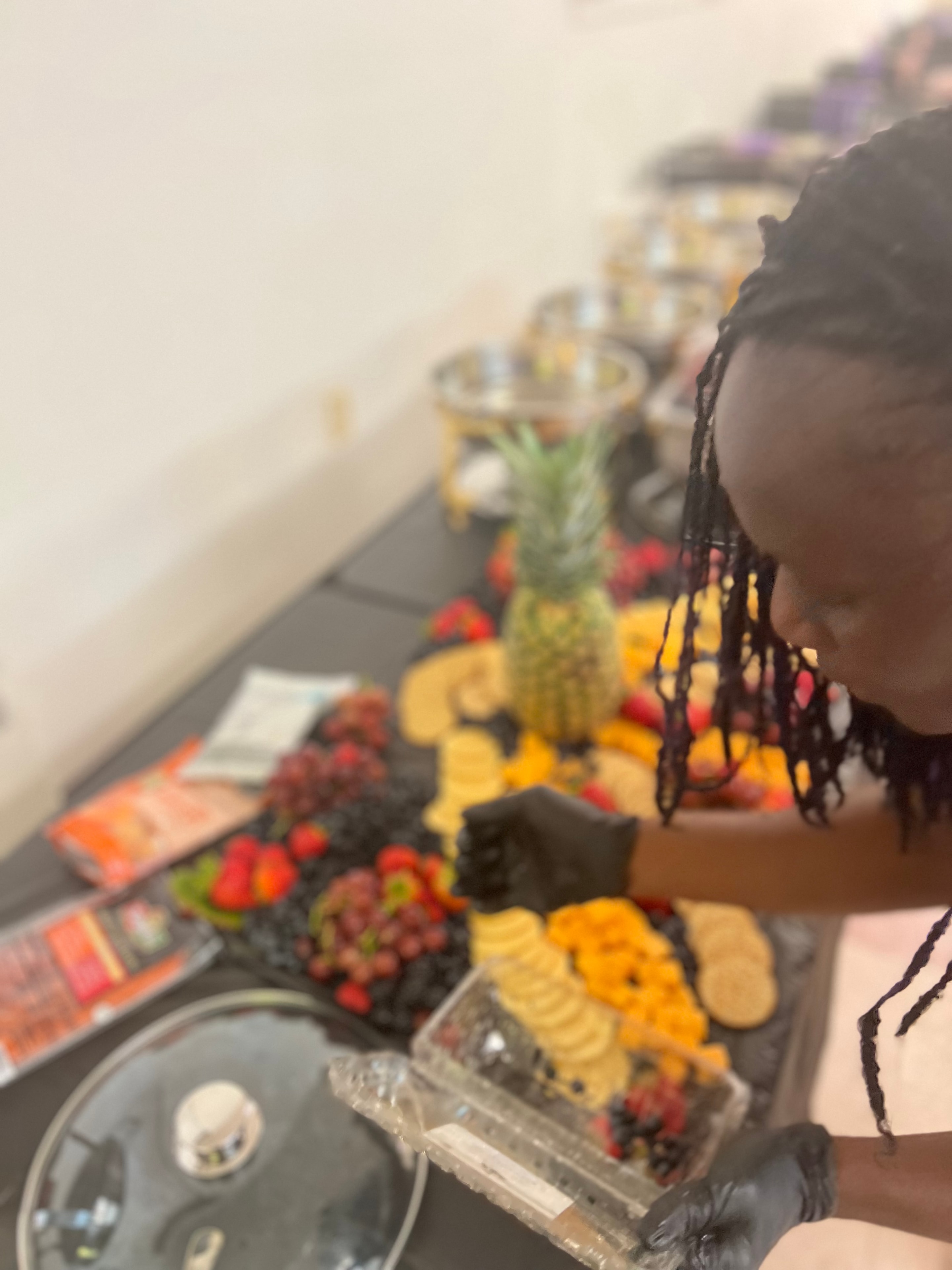 Dr. Bea arranging a grand fruit and charcuterie grazing table with pineapple centerpiece